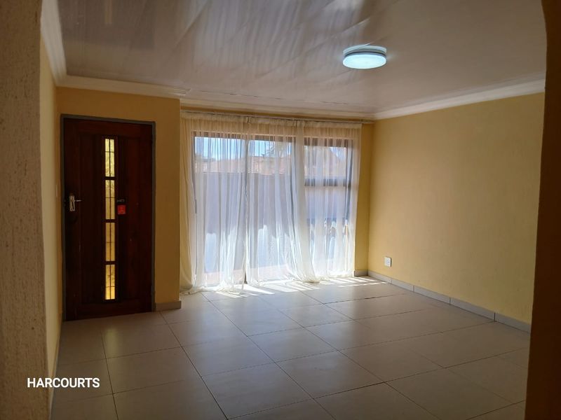 An empty living room featuring tiled flooring, a wooden entrance door, and a sliding glass door providing natural light.