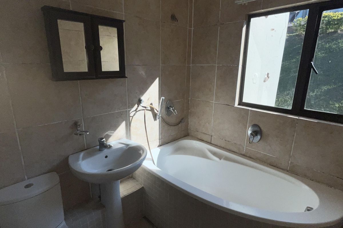 A functional bathroom featuring a pedestal basin, built-in bathtub, toilet, and wall-mounted medicine cabinet with neutral floor-to-ceiling wall tiling.