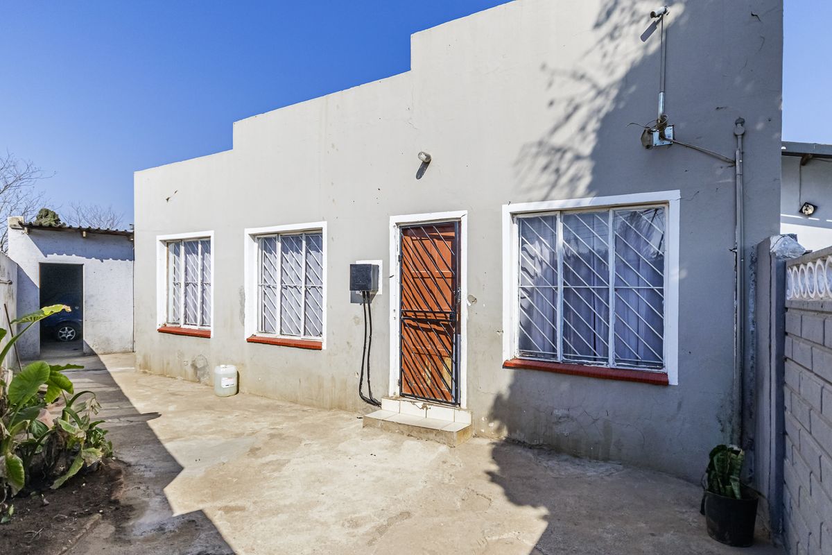 Rear exterior view of the house featuring concrete paving, security bars on windows, and a security gate at the entrance.