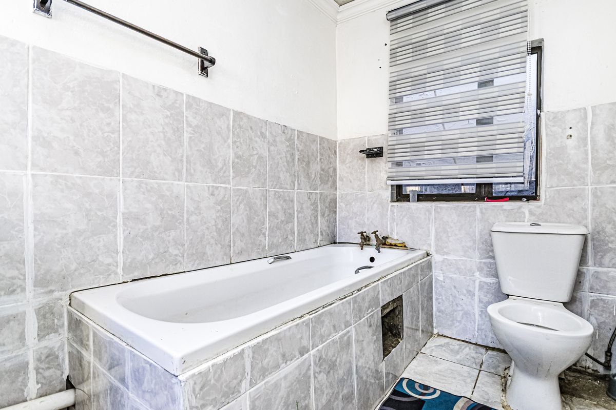 A dated bathroom featuring a built-in bathtub, toilet, and tiled finishes, requiring renovation to update the fixtures and address visible wear.