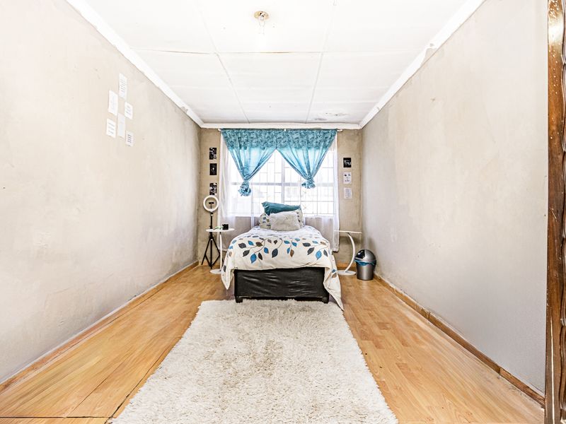 A bedroom featuring laminate flooring and a window, currently requiring cosmetic updates to the walls and ceiling to improve the overall finish.