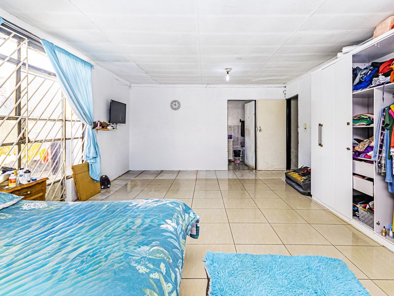 Spacious bedroom featuring tiled flooring, a large built-in wardrobe, and security bars on the windows.