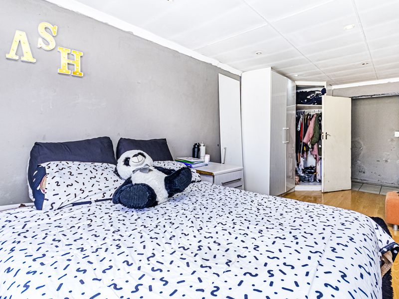 A bedroom featuring laminate flooring, built-in wardrobe storage, and recessed ceiling lighting, requiring cosmetic updates to the wall finishes and ceiling.