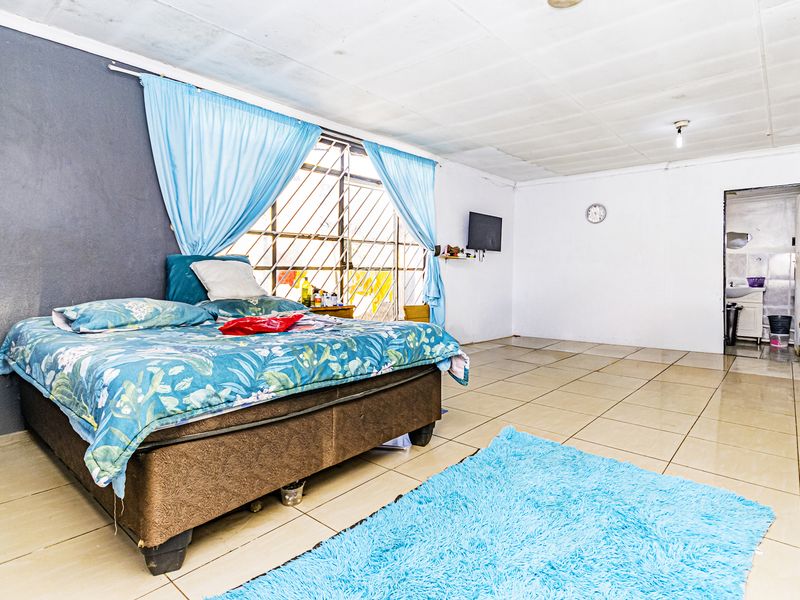 Spacious bedroom featuring tiled flooring, security bars on the window, and direct access to an adjoining bathroom area.