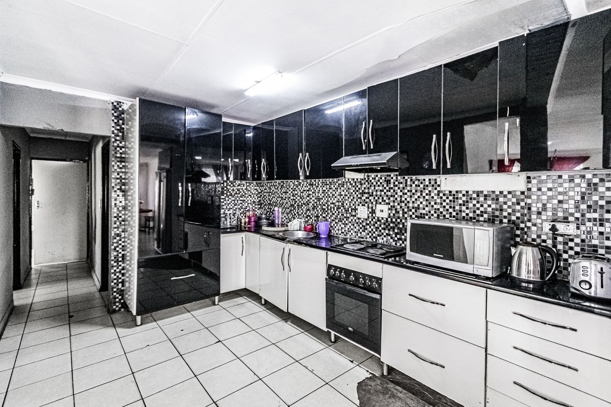 Kitchen featuring high-gloss black and white cabinetry, mosaic tile backsplash, built-in oven, and hob, with visible ceiling and flooring wear.