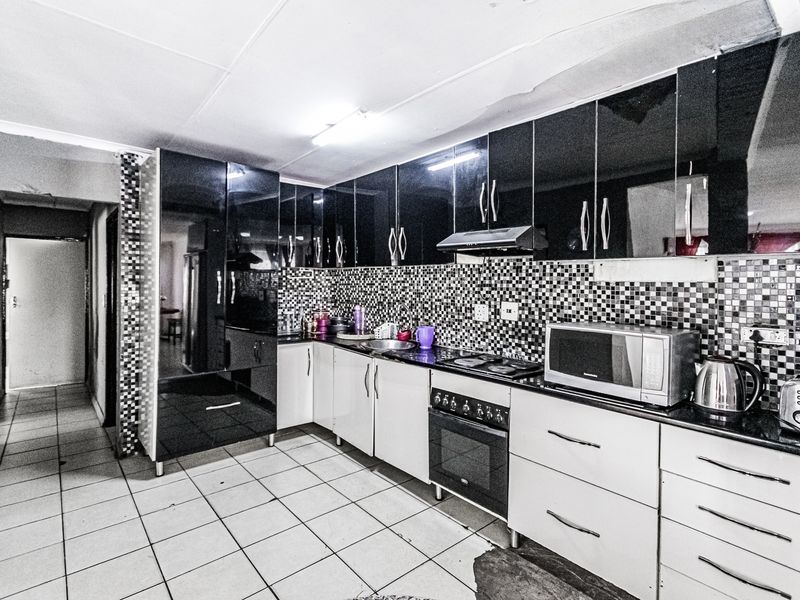 Kitchen featuring high-gloss black and white cabinetry, mosaic tile backsplash, built-in oven, and hob, with visible ceiling and flooring wear.