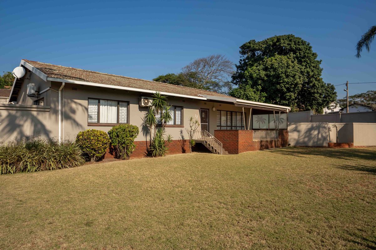 A well-maintained single-story house featuring a brick facade, tiled roof, and a covered patio area overlooking a spacious lawn.