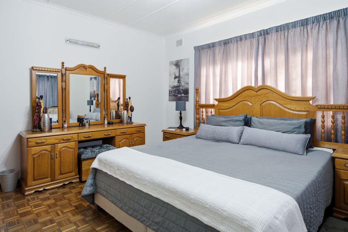 A well-maintained bedroom featuring classic parquet flooring, neutral walls, and functional window treatments, offering a comfortable and traditional living space.
