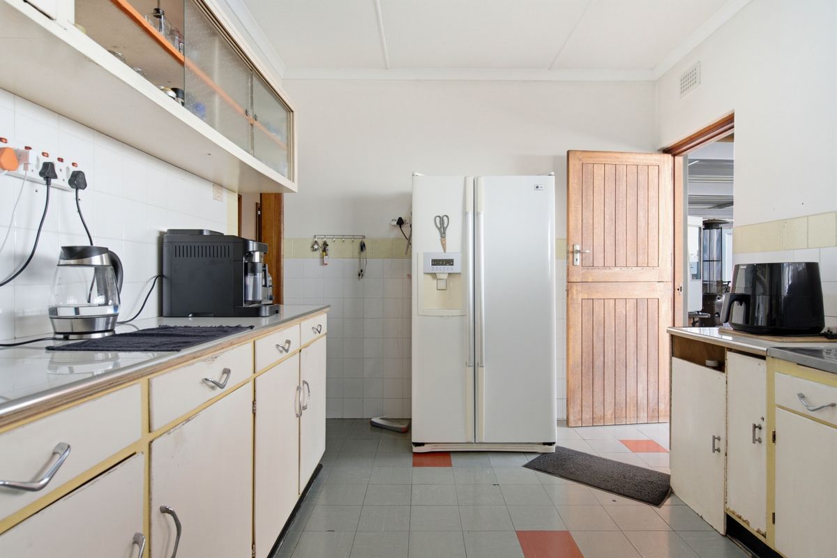 A functional kitchen featuring dated cabinetry, tiled splashbacks, and tiled flooring, offering significant potential for a modern renovation.