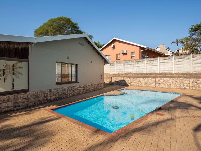 Outdoor pool area featuring a paved deck, stone-clad exterior wall, and secure perimeter fencing.
