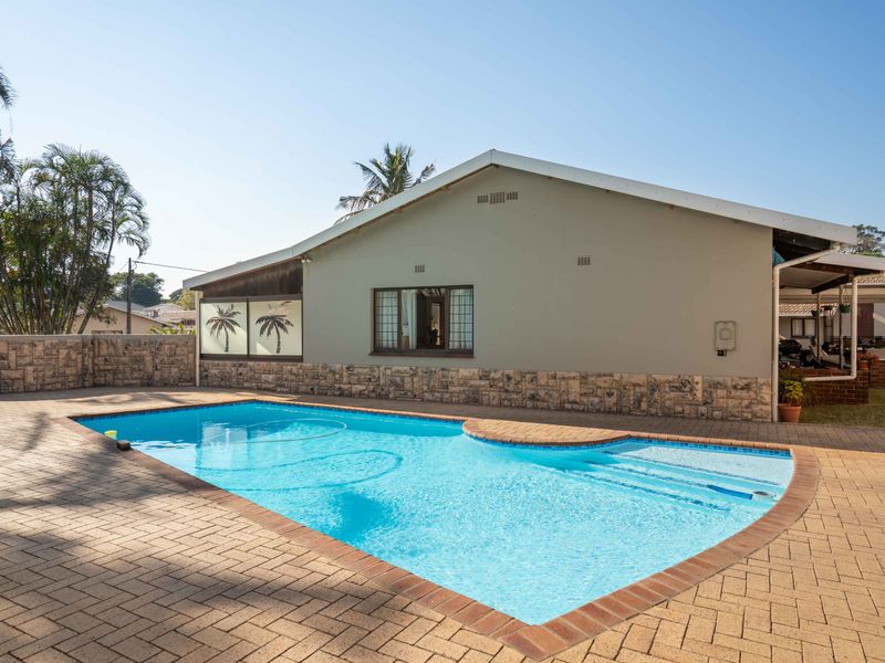 A well-maintained outdoor pool area featuring a paved deck, stone-clad exterior wall, and clear swimming pool.