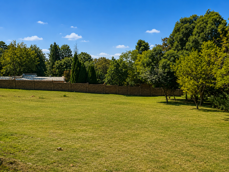 A spacious, well-maintained residential garden featuring a brick boundary wall and mature trees, offering a private and peaceful outdoor setting.