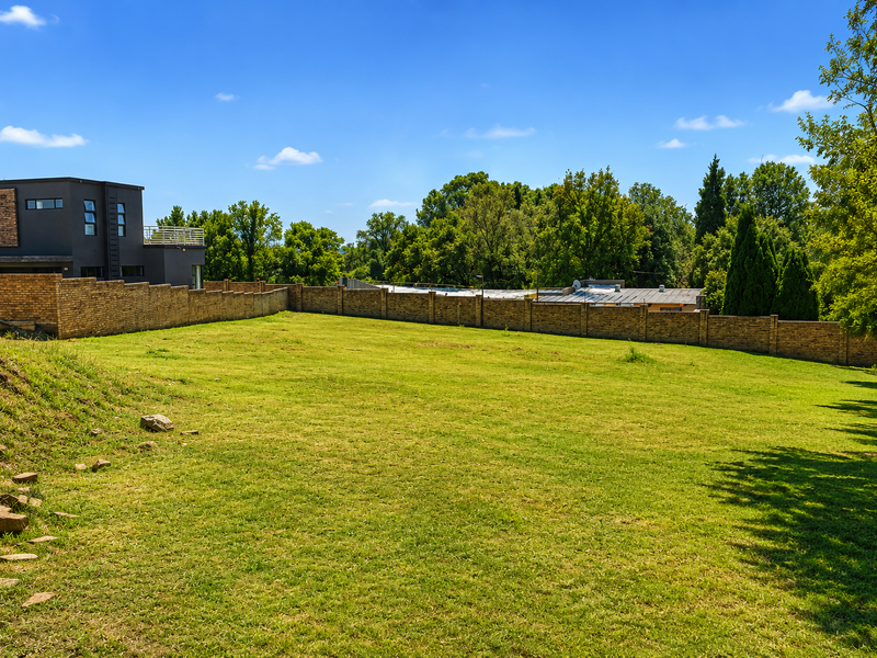 A spacious, well-maintained residential plot featuring a manicured lawn and a secure brick boundary wall, offering a clear view of the surrounding neighborhood.