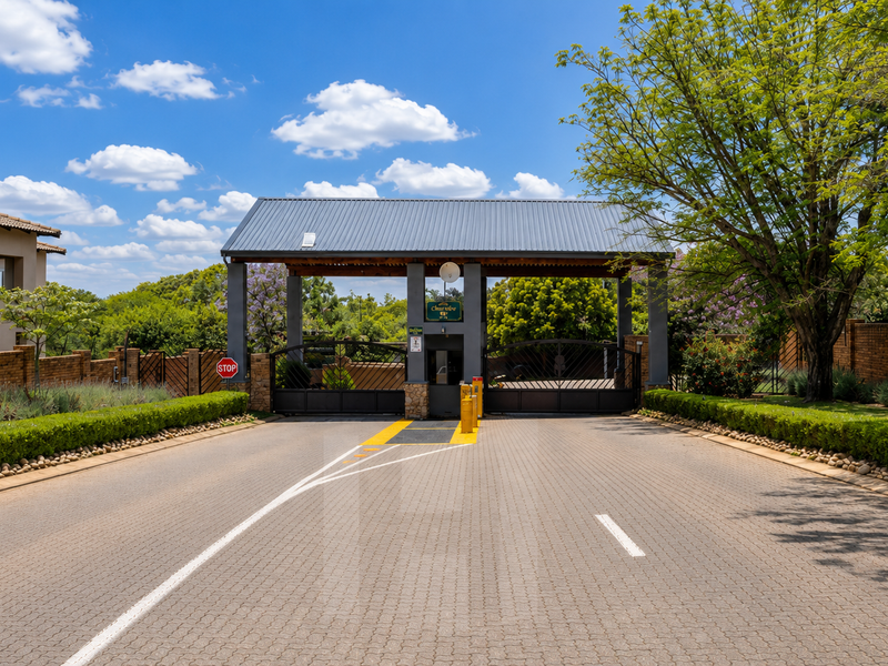 A well-maintained gated security entrance for the residential estate, featuring paved access, metal gates, and established perimeter landscaping.