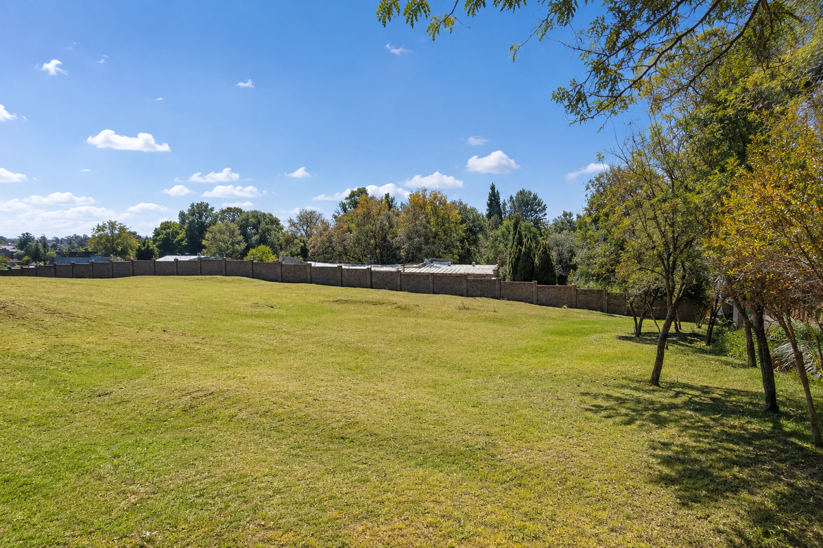 A spacious, well-maintained residential plot featuring a lush green lawn, mature trees, and a secure perimeter brick wall.