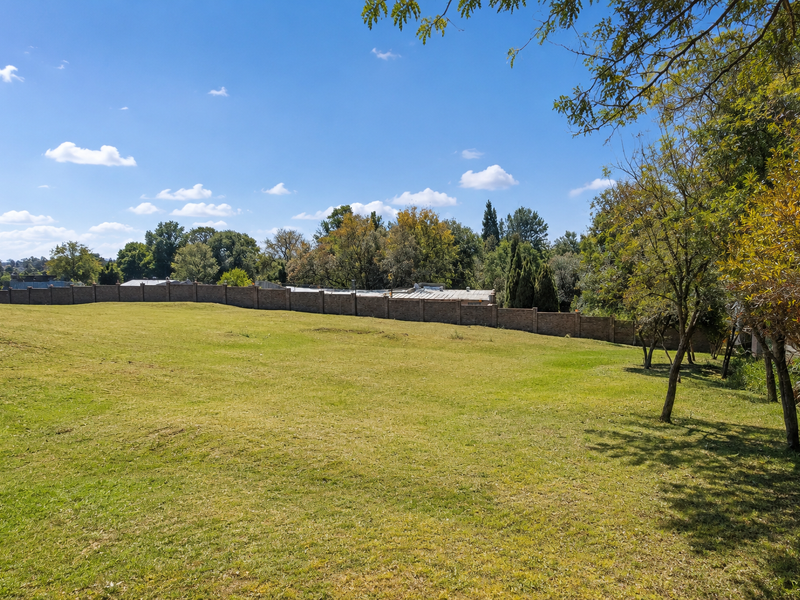A spacious, well-maintained residential plot featuring a lush green lawn, mature trees, and a secure perimeter brick wall.