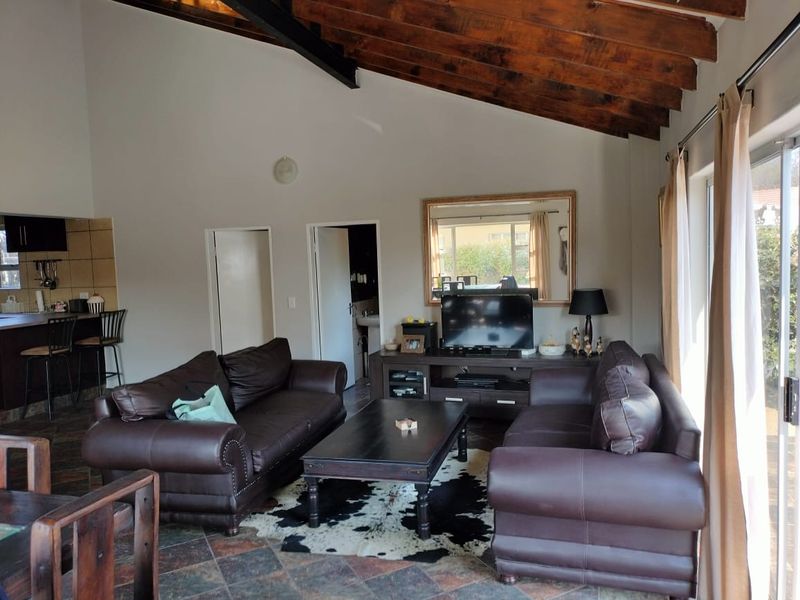 Open plan living area featuring high vaulted ceilings with exposed timber beams, tiled flooring, and direct access to the outdoors via sliding glass doors.