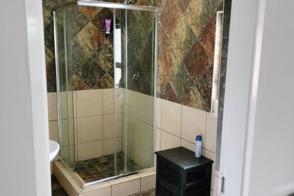 A functional bathroom featuring a corner shower enclosure, pedestal basin, and toilet with decorative tiled wall finishes.