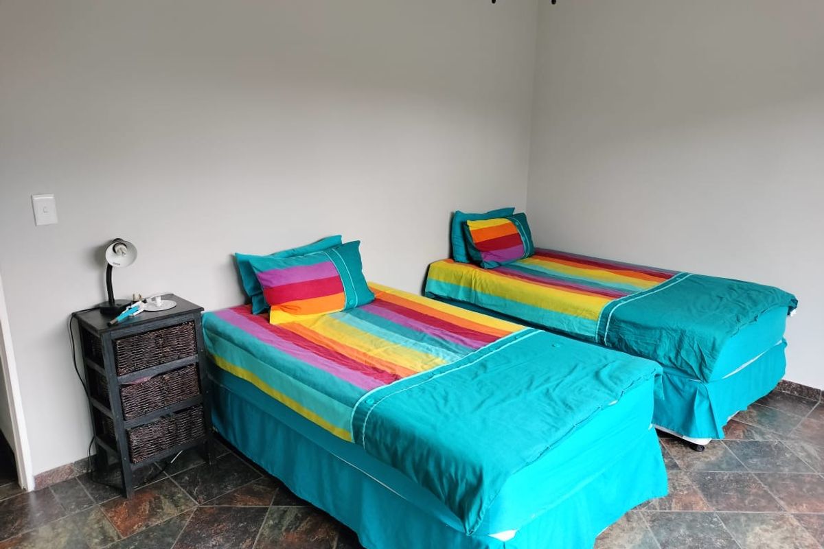 A bedroom featuring tiled flooring and a ceiling fan, currently furnished with two single beds.