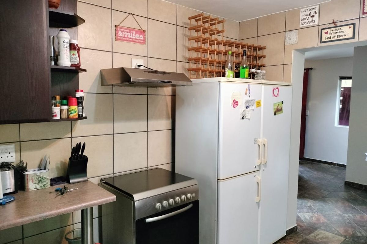 A functional kitchen area featuring tiled splashbacks, a stainless steel extractor fan, a freestanding oven, and built-in shelving units.