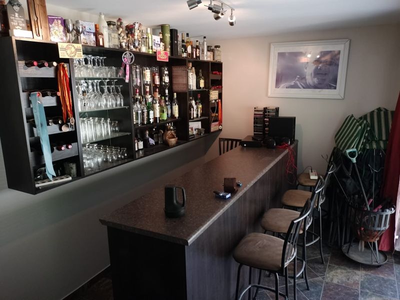 A dedicated home bar area featuring a built-in counter, extensive wall-mounted shelving for glassware and bottles, and durable tiled flooring.