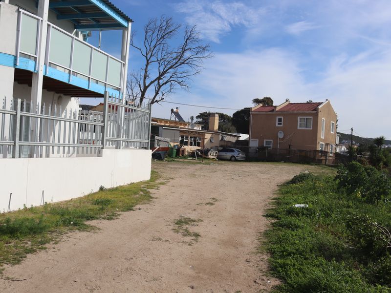 A view of the unpaved driveway and front access area of the residential property, featuring metal security fencing and a concrete retaining wall.