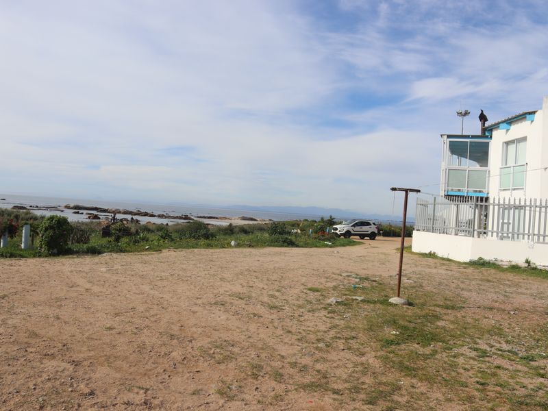 A view of the rear exterior of the property, featuring a sandy yard, metal fencing, and a balcony overlooking the coastal landscape.