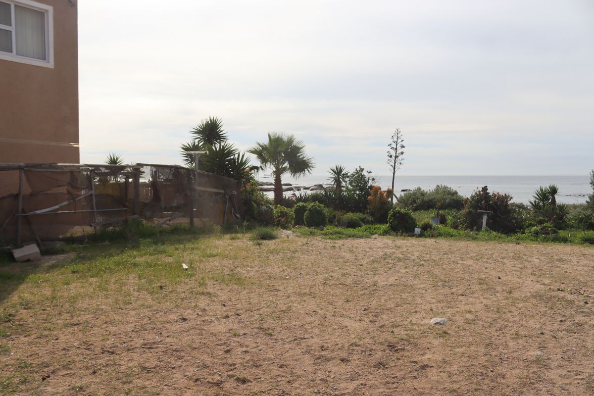 Rear exterior view of the property featuring a sandy garden area, established coastal landscaping, and ocean views.