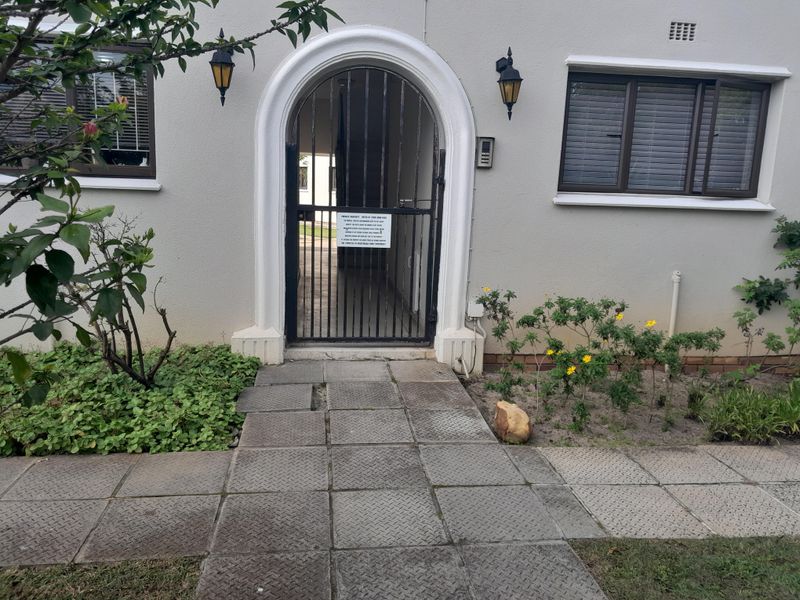 Exterior view of the apartment entrance featuring a secure metal gate, intercom system, and paved walkway leading to the front door.