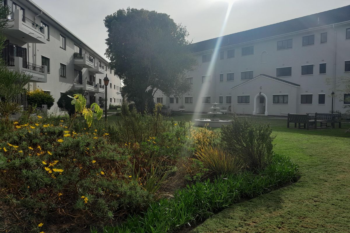 A well-maintained communal garden area featuring a central water fountain, landscaped flower beds, and views of the surrounding apartment building facades.