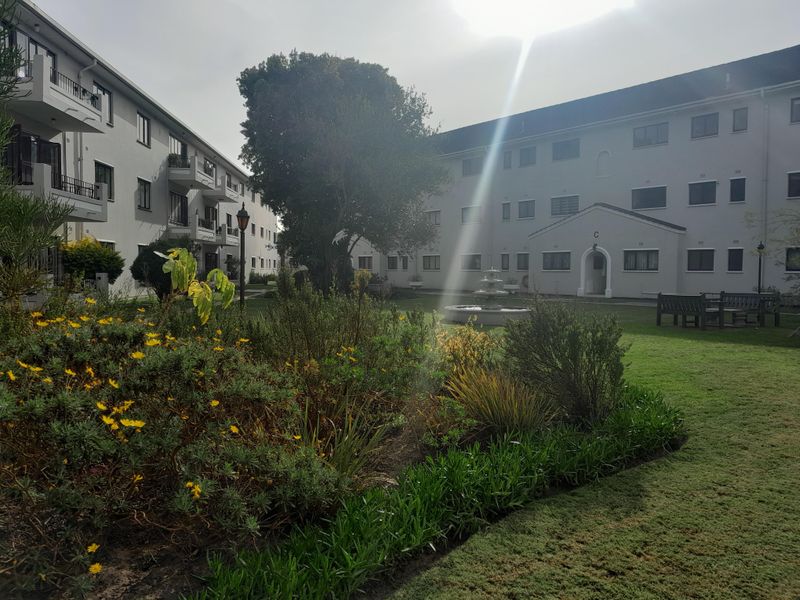 A well-maintained communal garden area featuring a central water fountain, landscaped flower beds, and views of the surrounding apartment building facades.