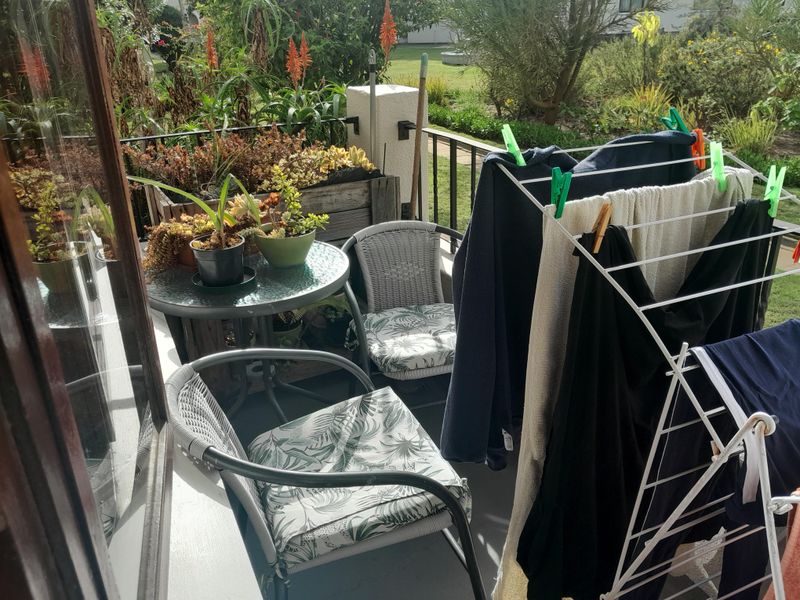 A functional balcony space featuring metal railings and concrete flooring, overlooking a garden area.
