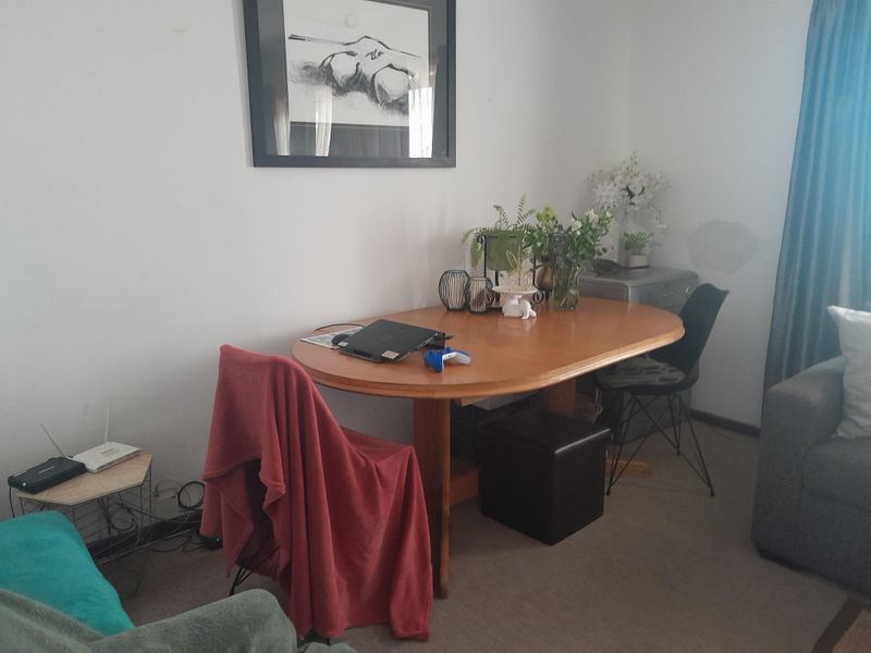 A living area featuring neutral carpeting and a visible wall blemish, offering a functional space for dining or relaxation.