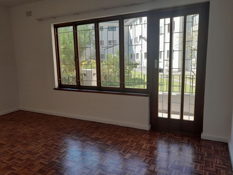 An empty living room featuring classic parquet flooring, large timber-framed windows, and a glass-paneled door providing access to the exterior.