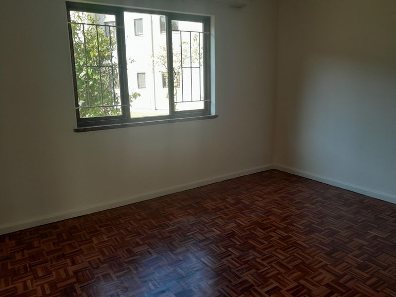 An empty bedroom featuring classic parquet flooring and a window fitted with security bars, offering a clean and neutral space.