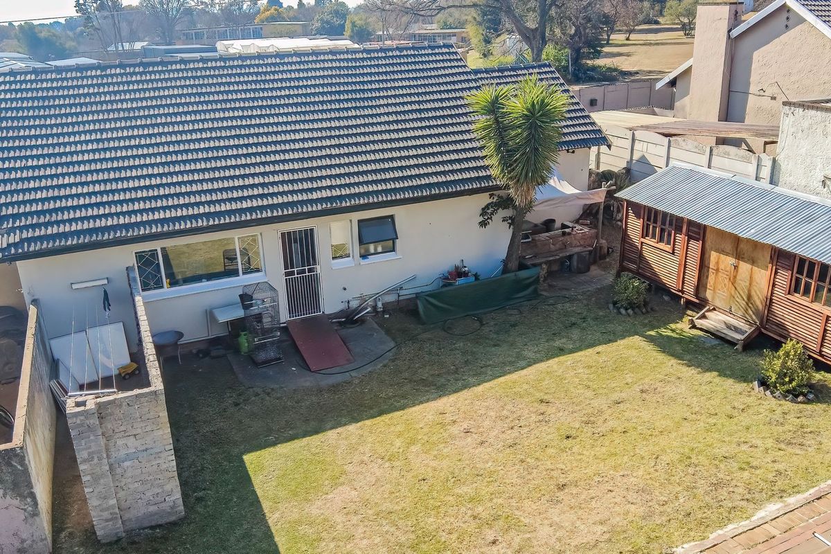 Aerial view of the rear property elevation featuring a tiled roof, garden space, a wooden shed, and a brick built-in braai area.