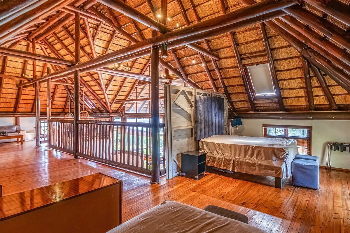 Spacious loft-style bedroom featuring exposed timber roof trusses, a traditional thatched ceiling, warm timber flooring, and a skylight for natural light.