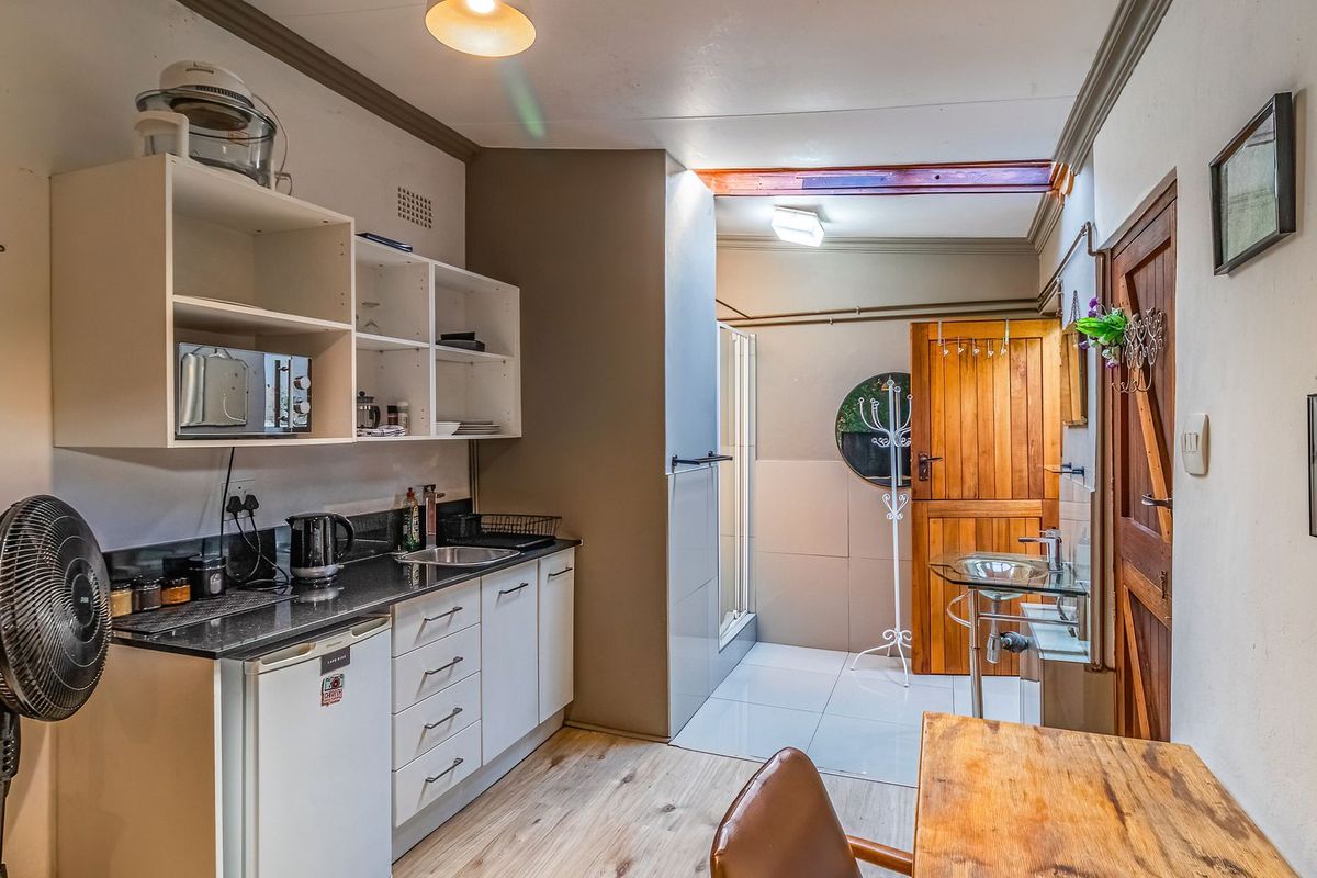A compact kitchen area featuring built-in cabinetry, laminate countertops, and a stainless steel sink, with an adjacent shower area and wooden door access.