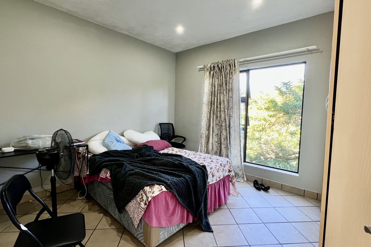 A functional bedroom featuring tiled flooring, a built-in cupboard, and a large window providing natural light and garden views.