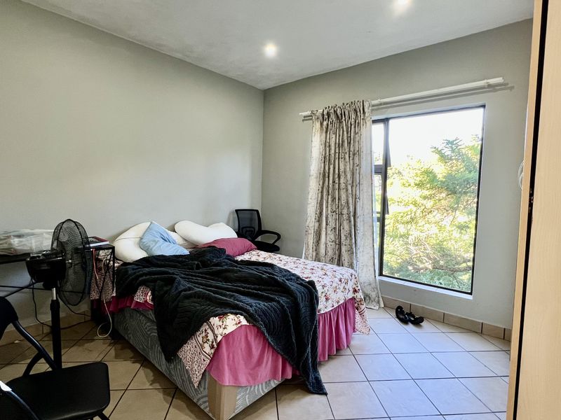 A functional bedroom featuring tiled flooring, a built-in cupboard, and a large window providing natural light and garden views.
