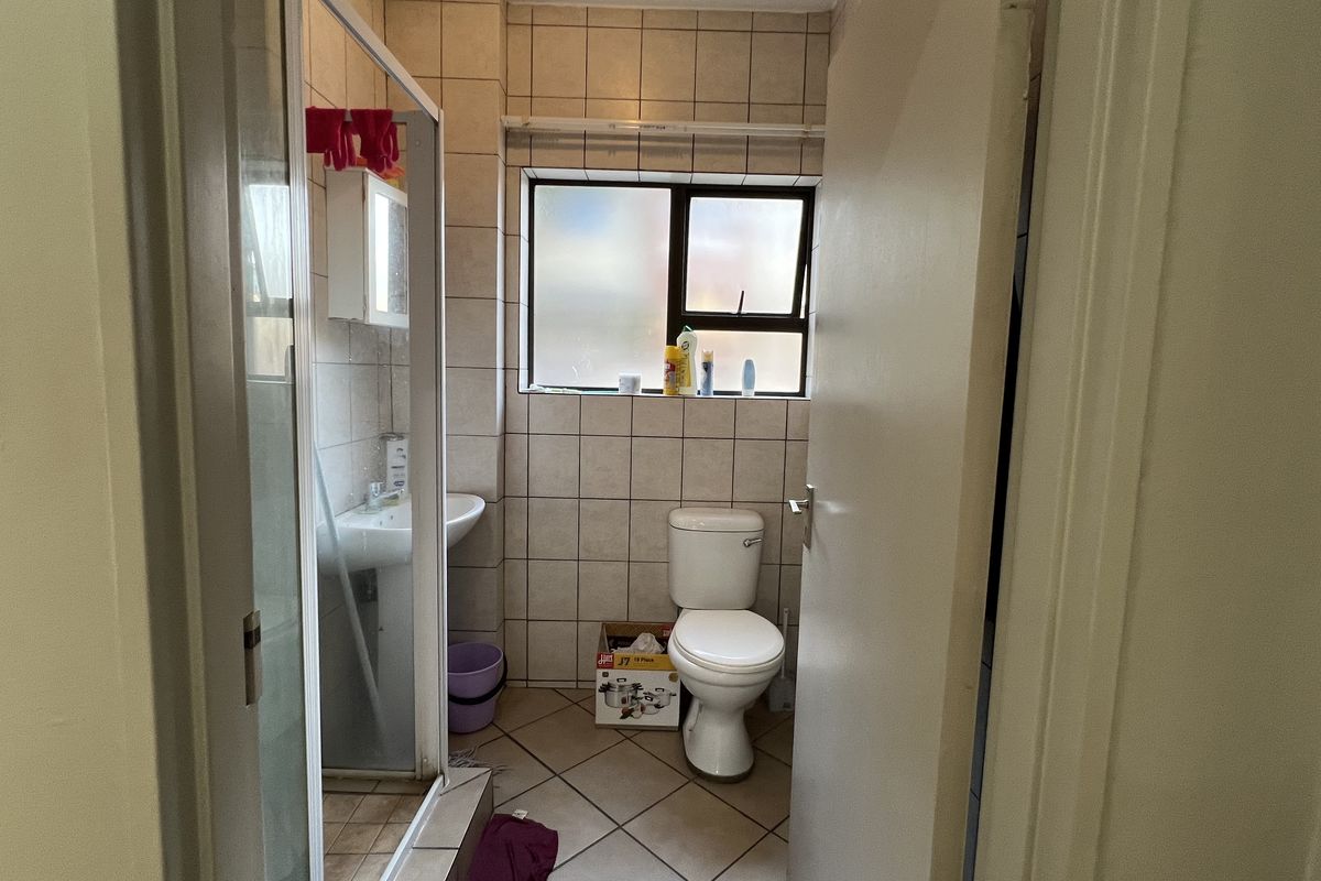 A functional bathroom featuring a shower enclosure, pedestal basin, and toilet, finished with neutral wall and floor tiling.