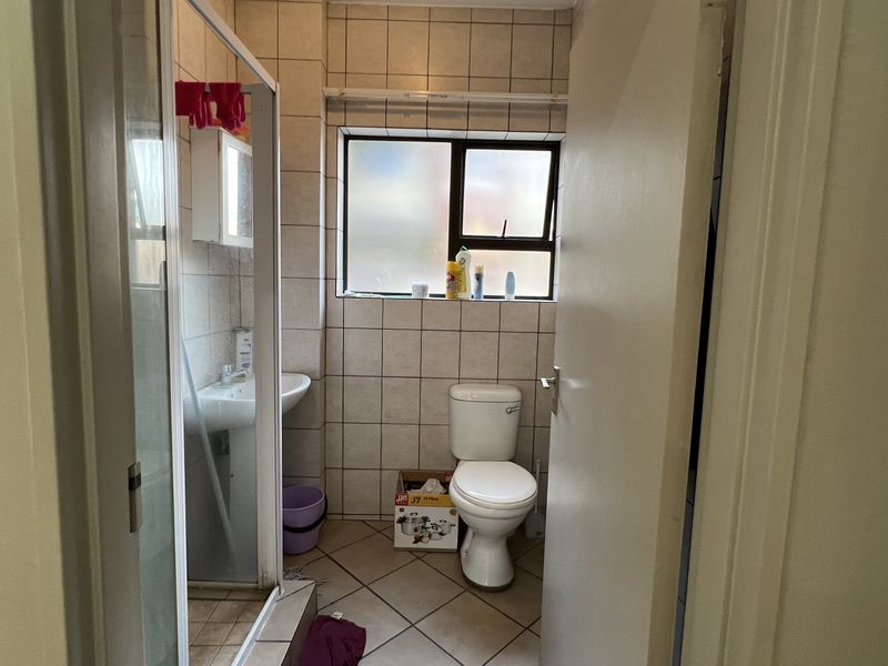A functional bathroom featuring a shower enclosure, pedestal basin, and toilet, finished with neutral wall and floor tiling.