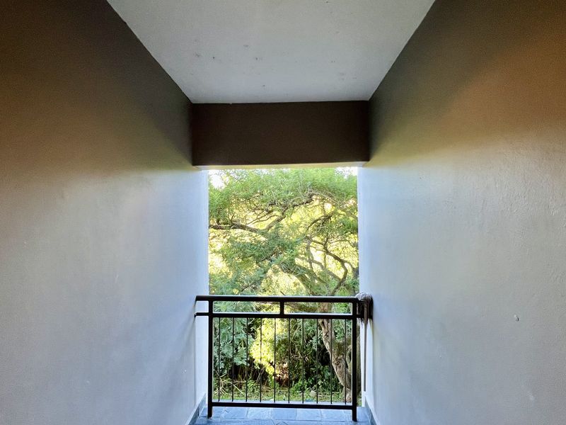 A simple balcony area featuring a metal balustrade and tiled flooring, offering a view of surrounding trees.