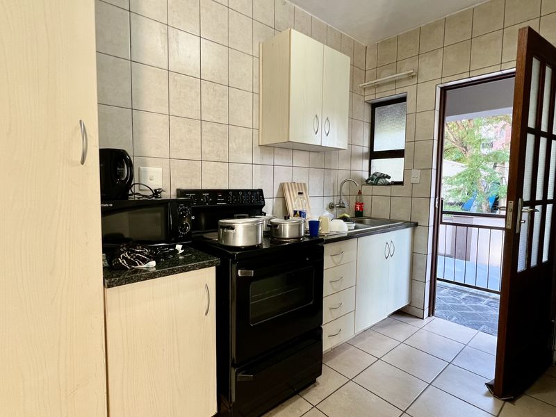 A functional kitchen featuring tiled walls, built-in cabinetry, a freestanding stove, and direct access to an outdoor balcony area.