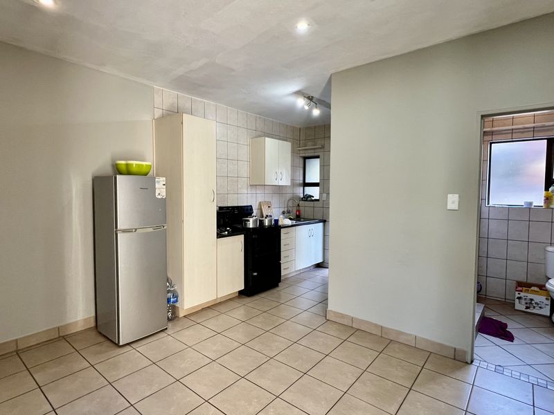 Open-plan kitchen area featuring tiled flooring, built-in cabinetry, and a tiled backsplash, with an adjacent view into a tiled bathroom space.