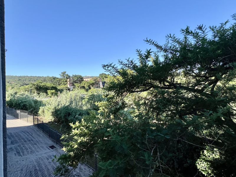 A scenic outdoor view overlooking a lush green landscape with a paved walkway and wire fencing visible below.