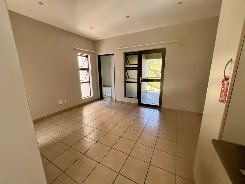 An empty, neutrally painted living area featuring tiled flooring, recessed lighting, and direct access to an outdoor balcony through an aluminium door.