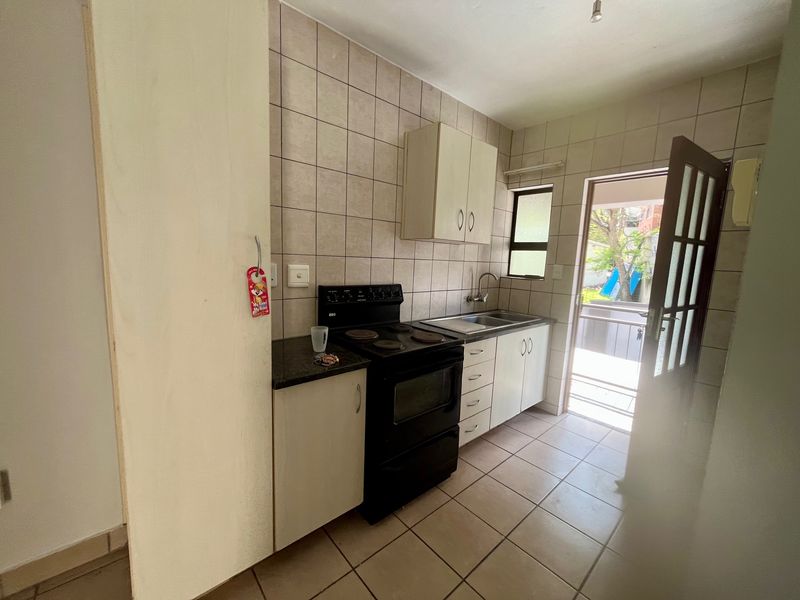 A functional kitchen featuring tiled flooring, a tiled backsplash, built-in cabinetry, and a freestanding stove, with direct access to an outdoor area.