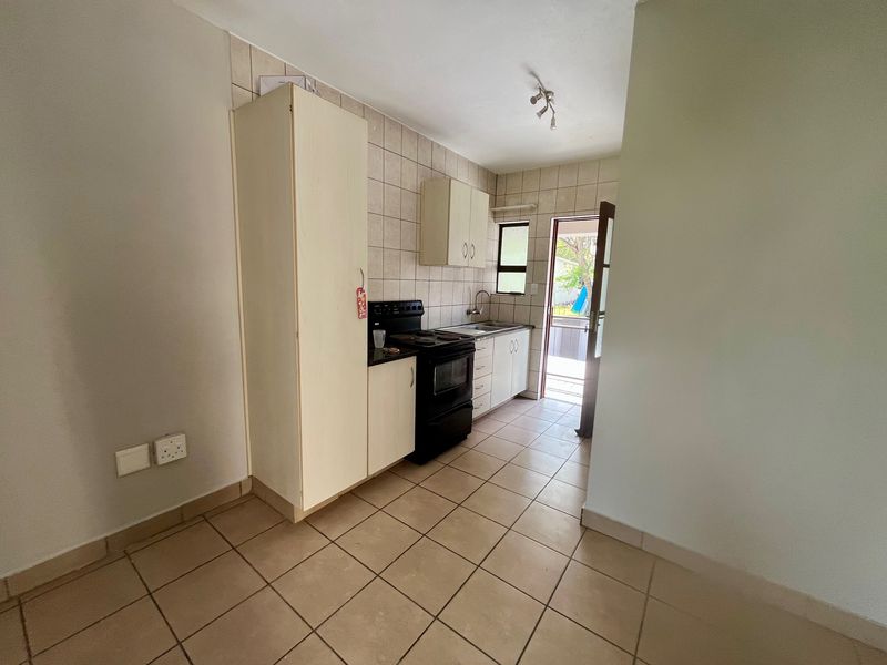 A functional kitchen featuring tiled flooring, a tiled backsplash, built-in cabinetry, and a freestanding stove, with direct access to an outdoor area.