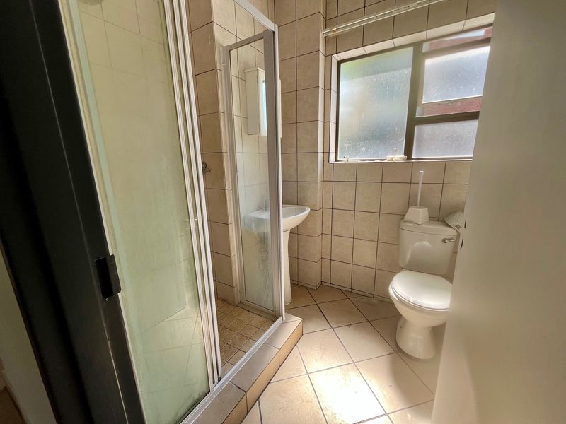 A functional bathroom featuring a shower enclosure, pedestal basin, and toilet with neutral wall and floor tiling.